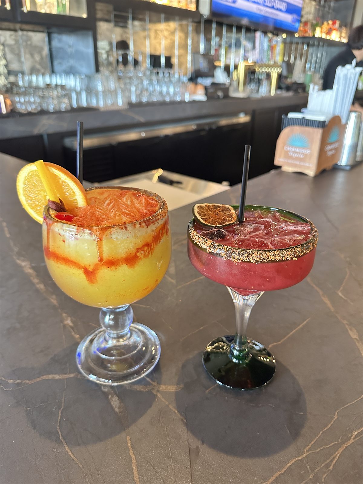 Frozen mango margarita and berry margarita side by side on a marble bar top