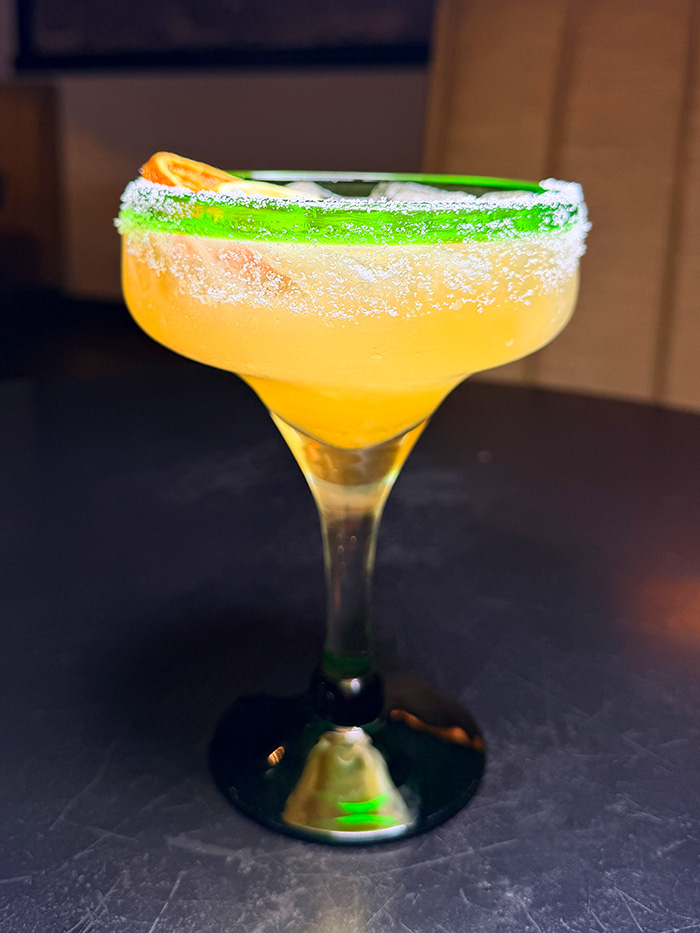 Classic margarita in a coupe glass with green sugar rim and orange citrus slice
