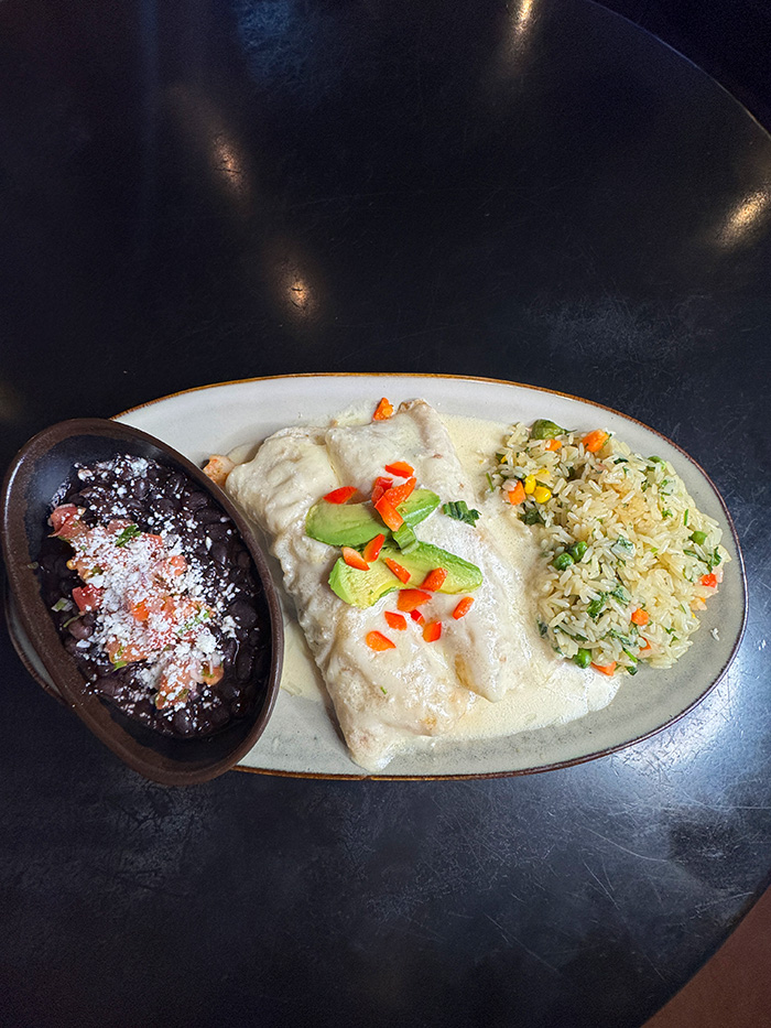 Seafood enchiladas in creamy white sauce with avocado, cilantro rice and black beans