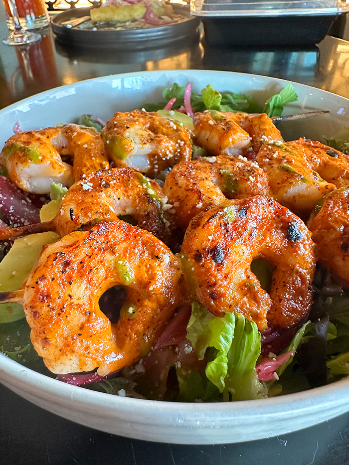 Chargrilled shrimp skewers piled over mixed greens, avocado and cotija