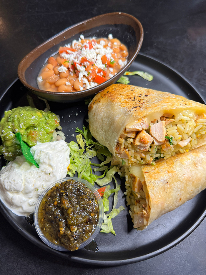 Grilled chicken burrito cut open with charro beans, guacamole and salsa verde