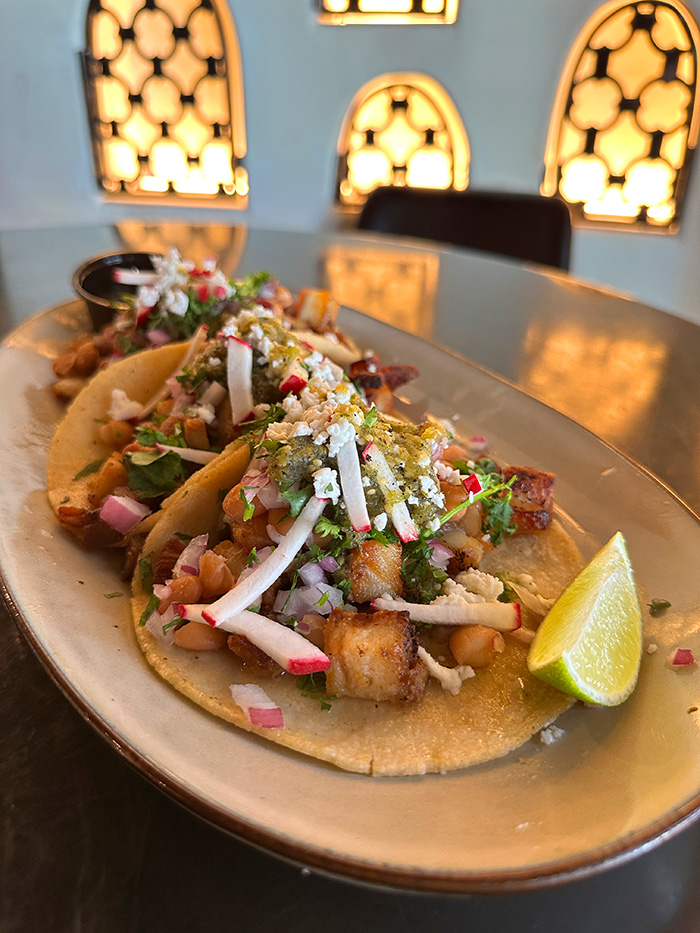 Chicharrón tacos with crispy pork belly, beans, radishes and queso fresco on an oval plate