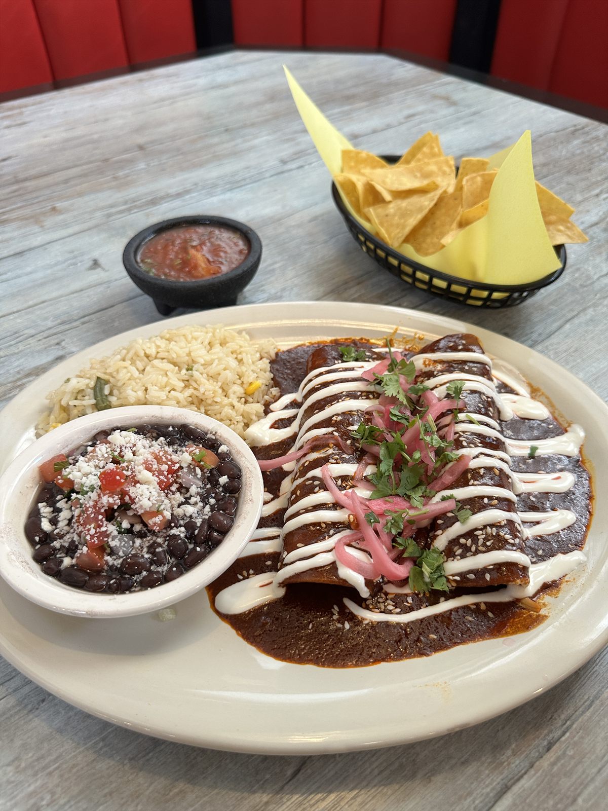 Enchiladas in smoky red sauce topped with crema, pickled onions and sesame with rice and beans