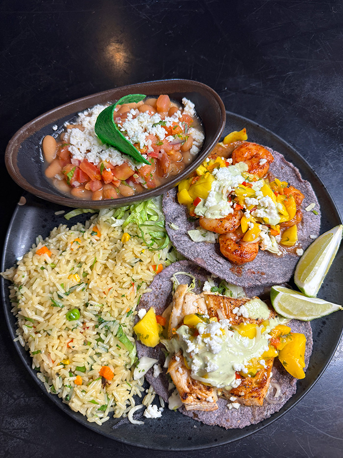 Grilled shrimp and fish tacos on blue corn tortillas with mango slaw and avocado crema