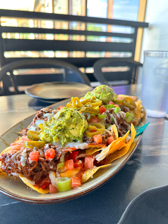 Loaded super nachos with shredded beef, guacamole, jalapeños, pico and crema on an oval platter