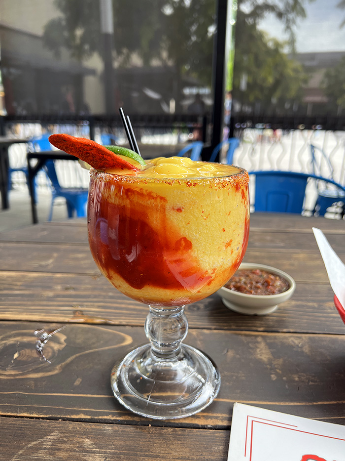 Frozen mangonada margarita with chili-salt rim on a wooden patio table
