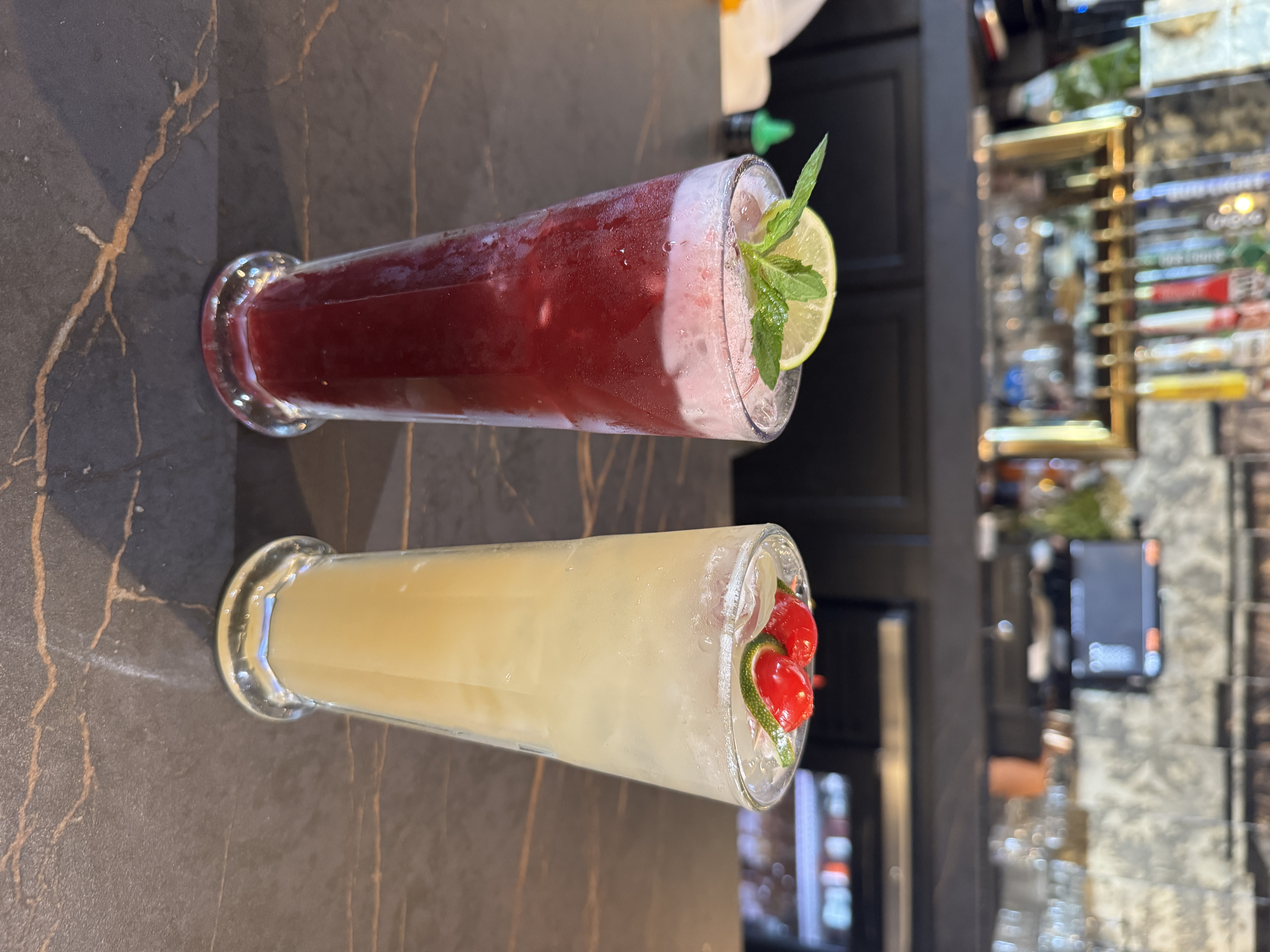 Two aguas frescas — deep-red jamaica and golden pineapple with peppers — on a marble bar top
