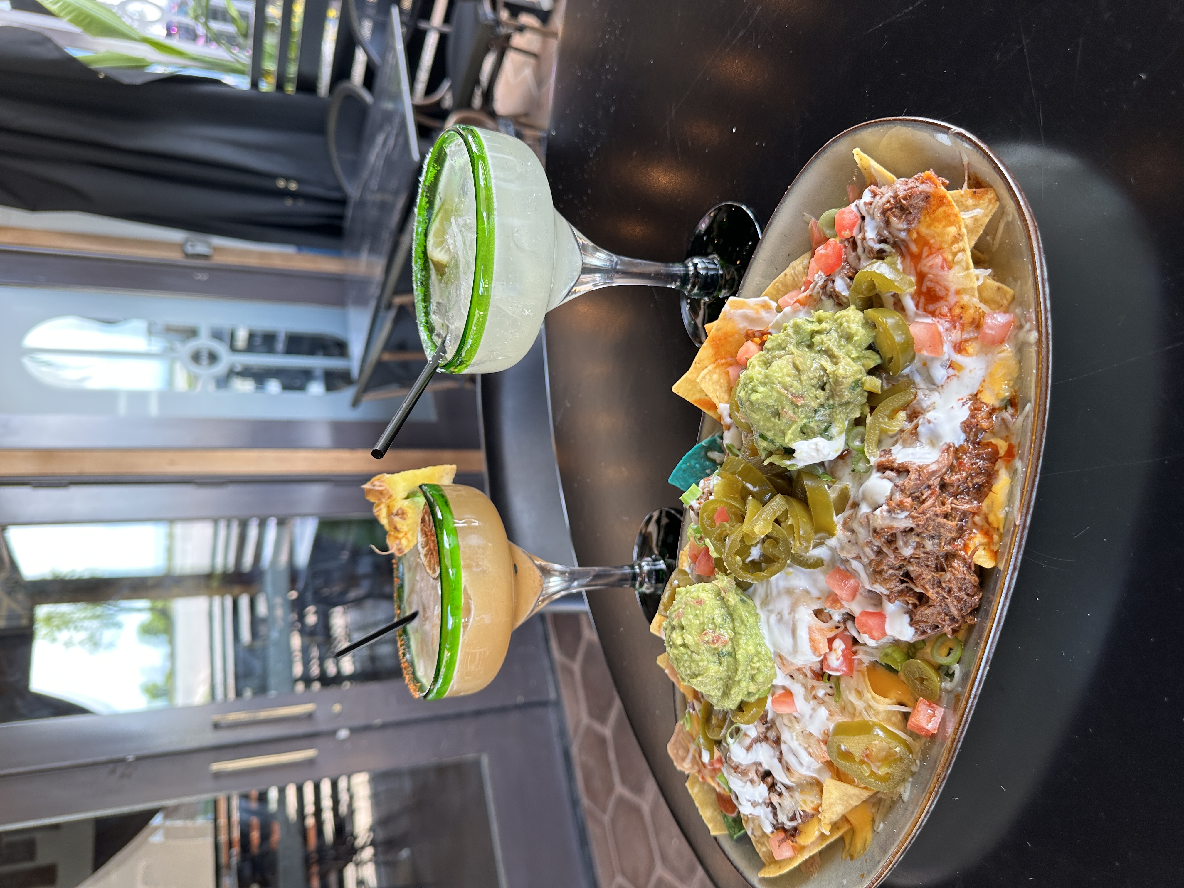Loaded birria super nachos with two frozen margaritas on a sunny patio table