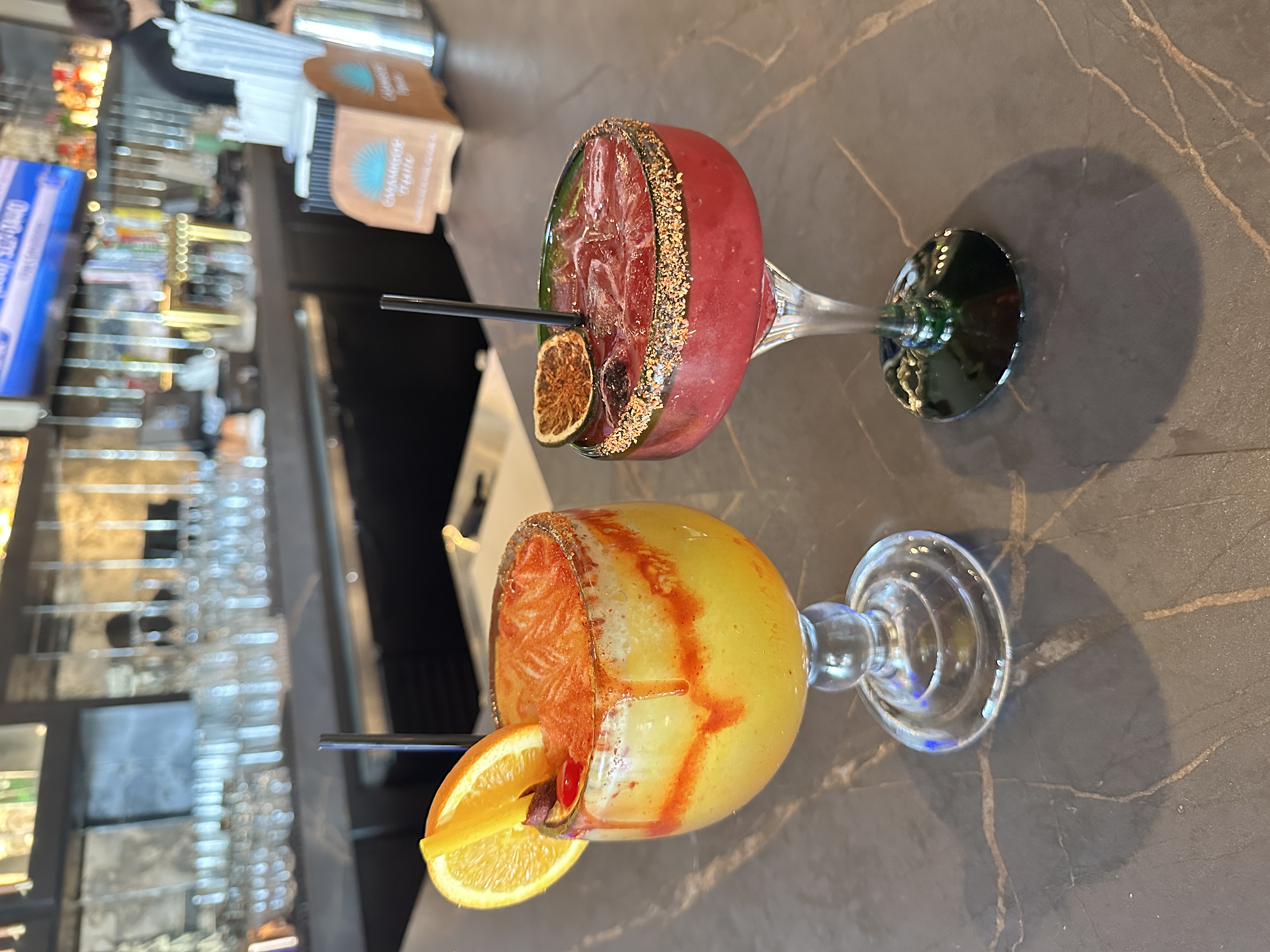 Two frozen margaritas — berry with chili-salt rim and mangonada with orange wheel — at the bar