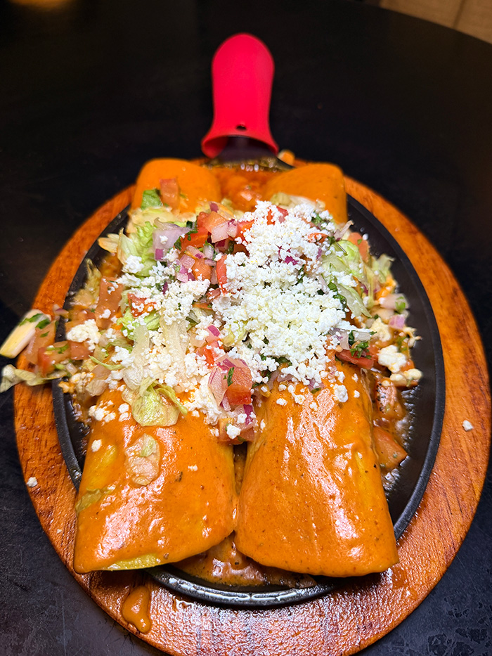 Enchiladas in chipotle cream sauce topped with pico and queso fresco on hot cast iron